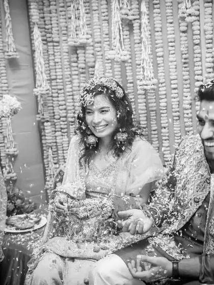 A classic Haldi moment captured in black and white. The couple is showered with flower petals by their laughing friends and family.