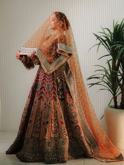 A full-length portrait of the bride in her intricately embroidered lehenga. The shot highlights the magnificent detail and craftsmanship of her wedding dress.