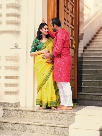An intimate moment captured on the steps of a temple. The husband-to-be gently touches his wife's baby bump as they share a loving gaze, their traditional outfits shining in the natural light.