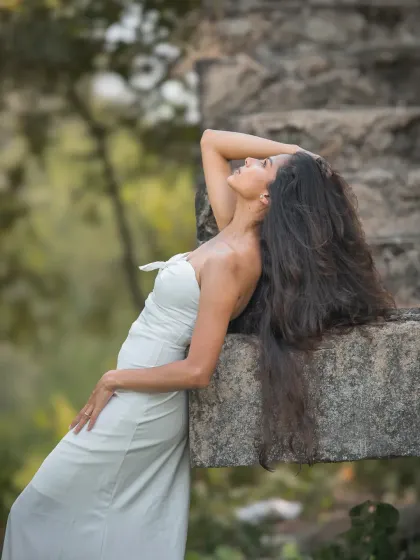 An editorial-style portrait with a dreamy, romantic feel. The model's pose and the natural, green backdrop create a stunning, high-fashion look.