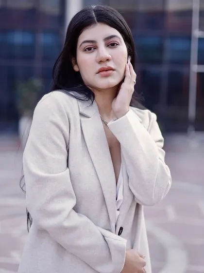 A close-up portrait against a modern architectural background, highlighting the model's serene expression and the texture of her coat.