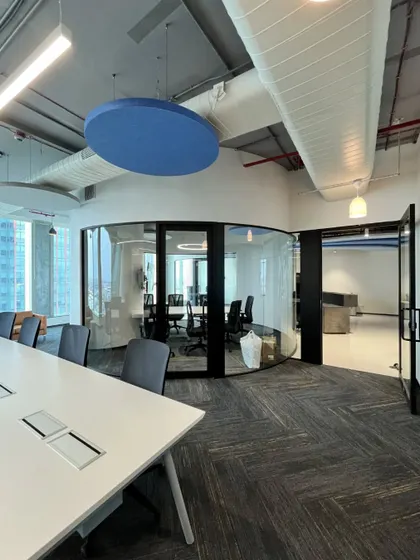 A curved glass meeting room at the Kissflow office provides acoustic privacy while maintaining an open feel. The circular acoustic panel on the ceiling helps to manage sound in this collaborative space.
