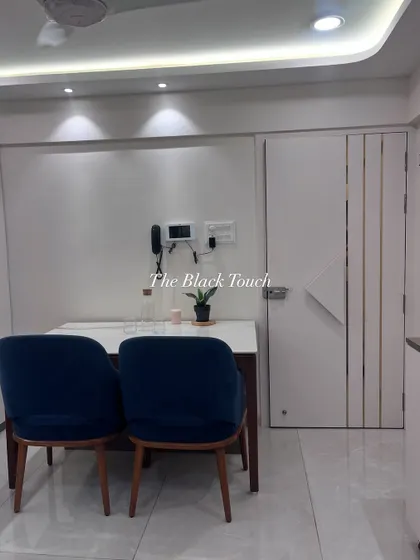 This image shows the dining area with a clean, minimalist aesthetic. The simple white table and dark blue chairs are complemented by a sleek, modern safety door, ensuring security without compromising on style.