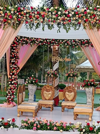 A beautiful outdoor mandap with pink and peach drapes, surrounded by lush greenery.