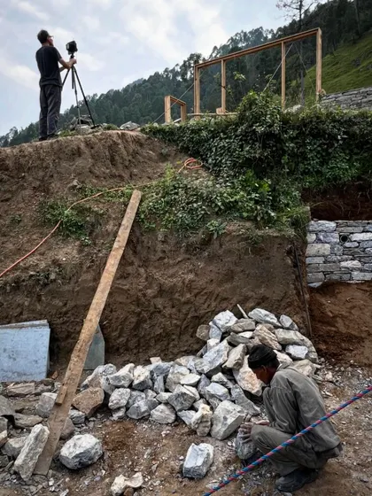 Documenting our work is a collaborative process. Here, a photographer frames a shot of the stone masons at work, capturing both the craft and the challenging terrain of our Himalayan site.
