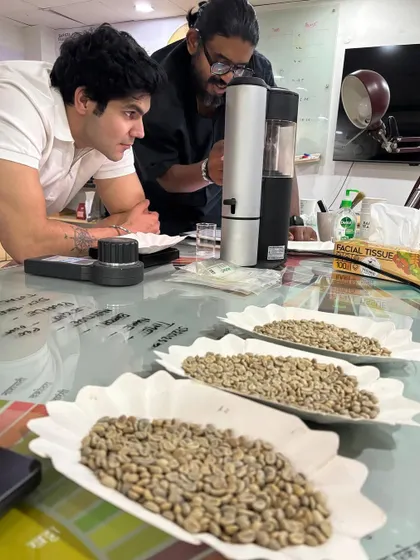 A trainer guiding a student through the process of sample roasting, explaining how to monitor the beans for optimal flavor development.