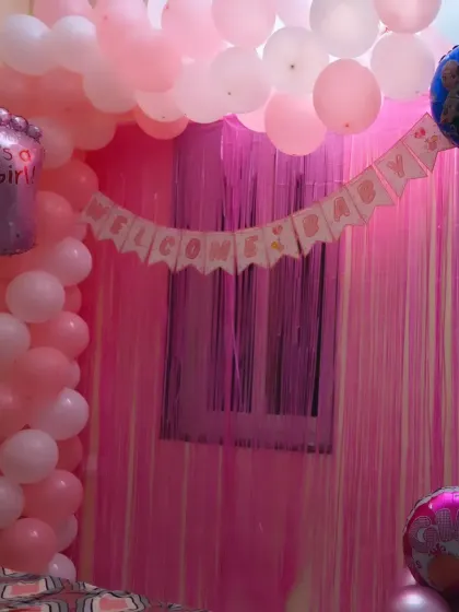 A classic bedroom setup for a baby girl's welcome. The pink and white balloon arch over the window, combined with a shimmer curtain, creates a beautiful and festive focal point.