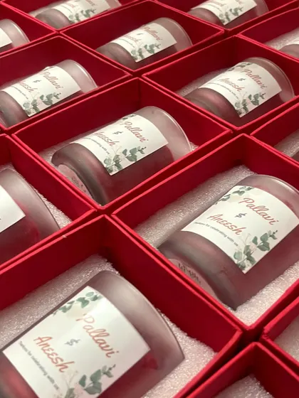 A snapshot of a completed bulk order of personalized wedding favor candles. Each candle features a custom label with the couple's names, neatly arranged in vibrant red gift boxes, ready to be shared with guests.