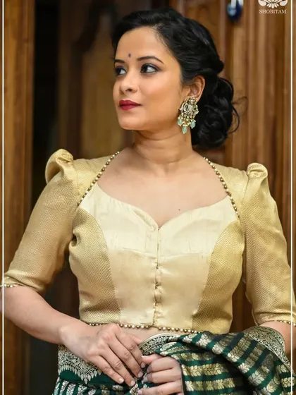 The model wears large, pearl-studded chandbali earrings that stand out against her elegant golden blouse. This is a perfect example of statement earrings elevating a classic look.
