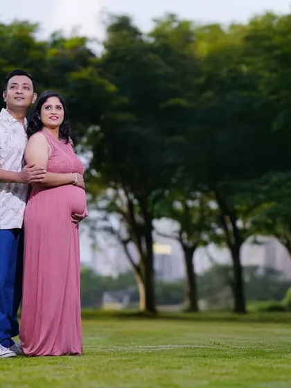 A wide shot of an expecting couple in a beautiful green park. This type of photo captures not just the couple, but also the serene and expansive environment of the outdoor location.