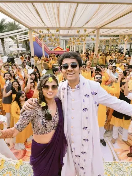 The couple and their friends celebrate with abandon at their Haldi ceremony, a wide shot capturing the energy of the crowd.