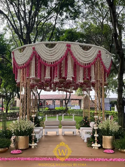 An absolutely breathtaking traditional mandap design. The structure is adorned with hanging garlands of pink and white rajnigandha, with brass urli bowls creating a stunning floral chandelier effect.