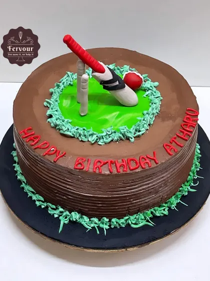 A chocolate-frosted cricket theme cake with a fondant bat, ball, and wickets. The red lettering for the birthday message adds a nice pop of color.
