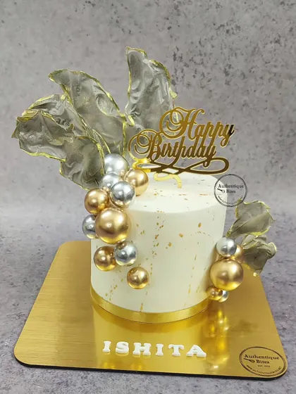 A glamorous silver and gold cake with translucent sails and a cascade of metallic spheres.