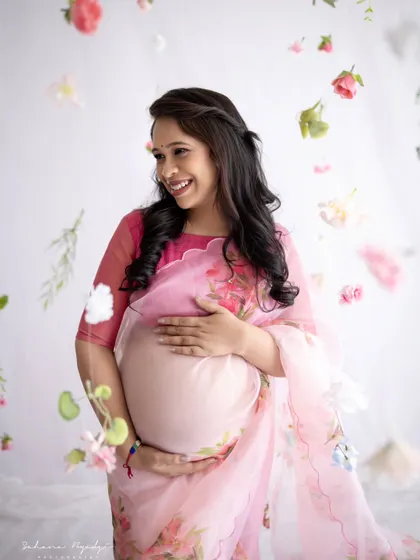 The joy on her face is infectious. This mom-to-be, dressed in a lovely floral saree, looks absolutely radiant as she smiles, surrounded by a delicate cascade of petals.