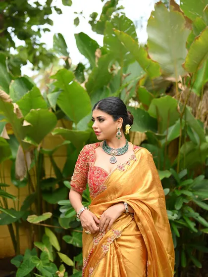 A stunning golden Kanjivaram tissue silk saree, paired with a vibrant red hand-embroidered blouse. A royal and timeless combination.