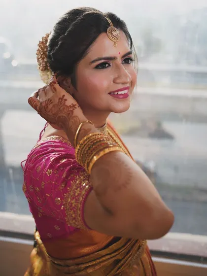 A happy bride glowing on her wedding day. This close-up shows her fresh and radiant makeup, with a bright smile and sparkling eyes. The traditional hairstyle adorned with flowers adds a classic South Indian touch.