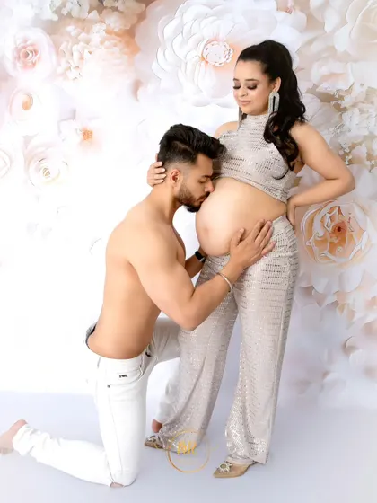 A tender moment with the father-to-be kissing the baby bump. This shot is from a high-fashion maternity session against a white paper flower wall.