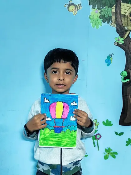 This student is excited to show his colorful hot air balloon drawing, set against a bright blue sky.