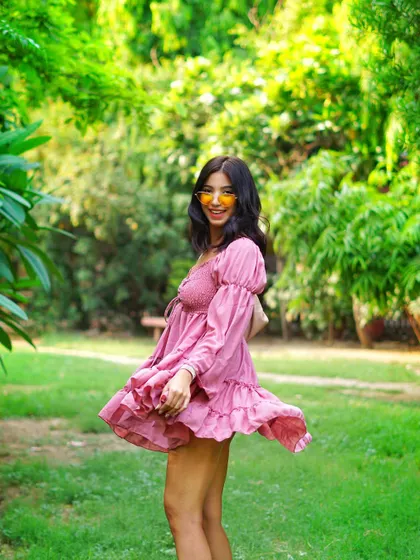 A smiling, over-the-shoulder glance that feels spontaneous and charming. The lush green background makes the pink dress stand out.