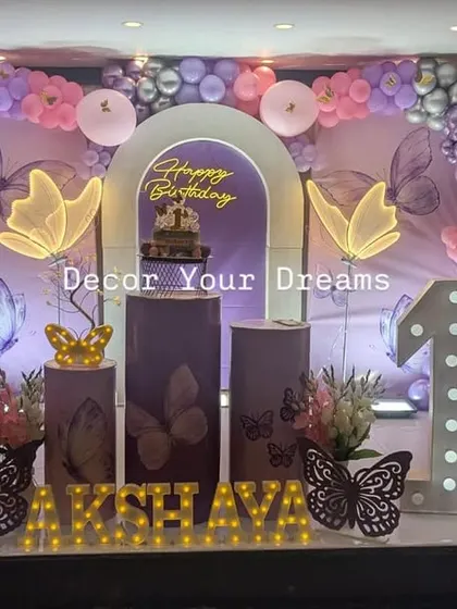 A butterfly themed first birthday party with a unique arched backdrop. The purple and pink color scheme is enhanced with glowing butterfly props.