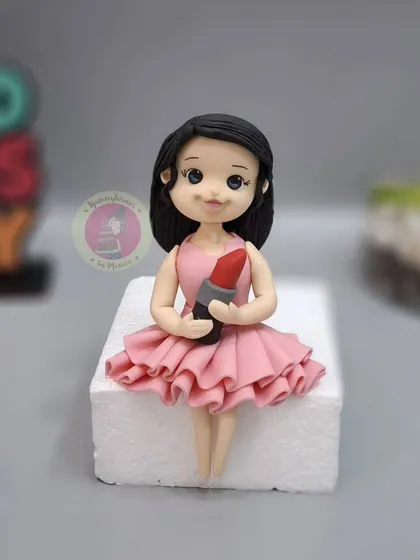 A custom fondant figurine of a girl holding a lipstick, created for a makeup-themed cake.