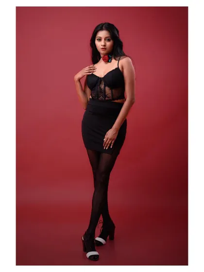 A full-body shot of a model in a glamorous black outfit. The pose is powerful and confident, set against a rich red background for maximum impact.