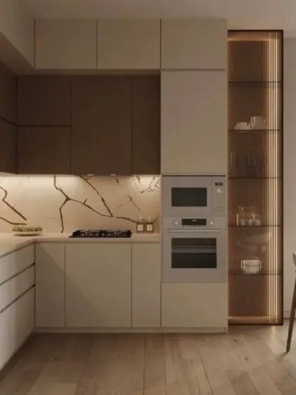 A corner view of a kitchen showing the seamless integration of appliances within the cabinetry. The design uses a neutral color palette and a striking marble backsplash, with a glass display cabinet for added visual interest.