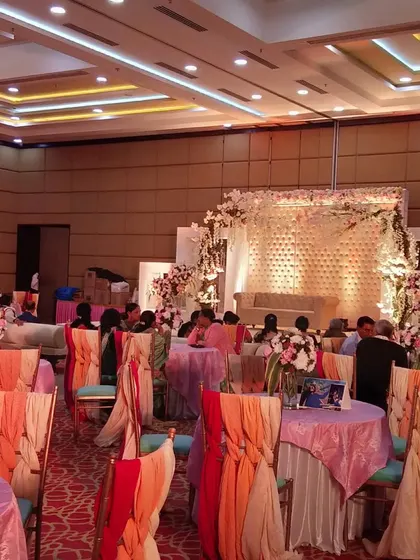 A pastel-themed indoor event with a focus on seating. The tables are covered in multi-colored pastel linens, and the chairs are decorated with flowing organza sashes in shades of peach and pink.