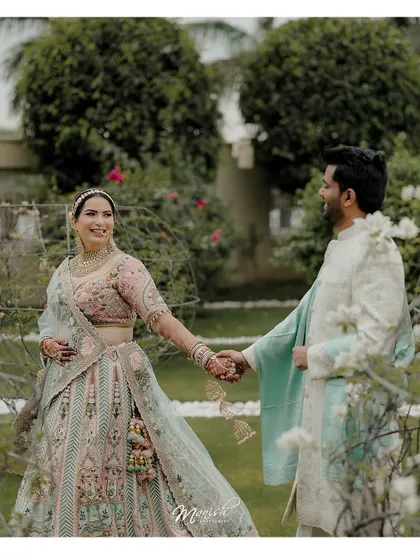A candid moment of the couple walking hand-in-hand through a lush garden, their smiles reflecting their happiness.