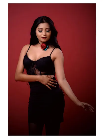A full-body shot of a model in a glamorous black outfit. The pose is powerful and confident, set against a rich red background for maximum impact.