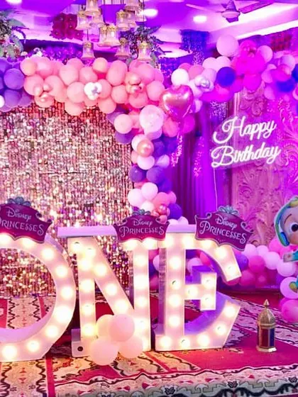 A vibrant Disney Princess and Cocomelon combined first birthday party. The decor is rich in pink and purple, with a sequin wall and "ONE" marquee letters.