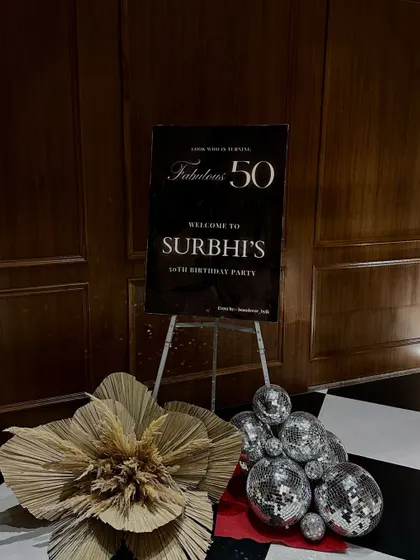 The welcome sign for a "Fabulous 50" birthday party. We set the disco theme right from the entrance with a stylish sign, disco balls, and a large dried palm leaf accent.
