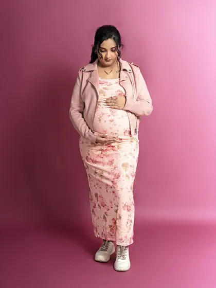A modern and stylish maternity look. The mom-to-be pairs a floral dress with a pink jacket and sneakers for a cool, contemporary portrait.