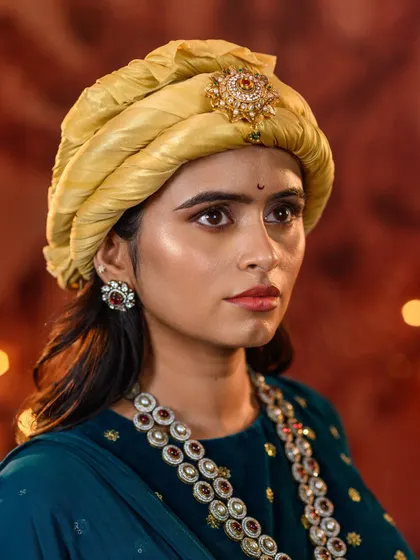 A close-up portrait capturing a softer, more contemplative expression. This highlights the detailed jewelry, the carefully wrapped yellow pagri, and the subtle makeup that completes the look.
