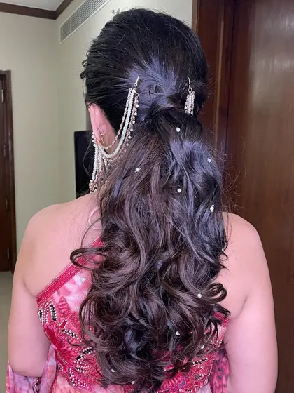A soft and romantic ponytail with curls, adorned with a chained pearl accessory for a touch of elegance.