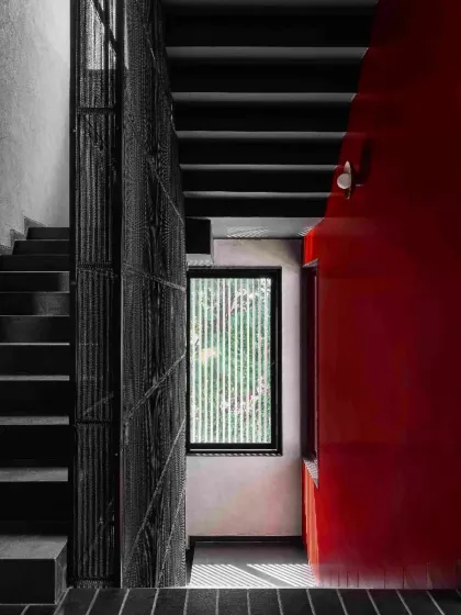 A staircase detail in Project 1374, where a bold red wall contrasts with the dark, textured metal screen and concrete steps. The composition is a study in material, color, and geometric form.
