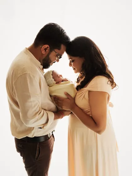 A classic family portrait with a newborn. The parents gaze at their baby with so much love, creating a serene and emotional image against a clean, white background.