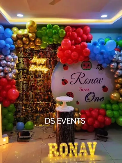 This ladybug-themed first birthday is perfect for a smaller, intimate celebration at home. The decor includes a colorful balloon arch against a sequin backdrop, a large light-up number "1", and a custom name sign.