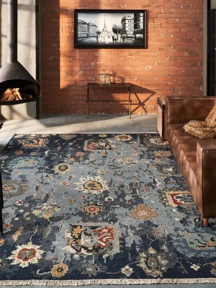 An industrial-loft style living room featuring a dark, patterned rug. The combination of leather furniture, a brick wall, and a modern fireplace creates a masculine and sophisticated mood.