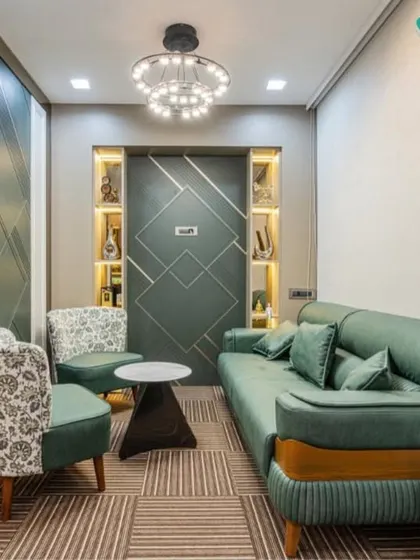 A view of the client lounge area, featuring a plush green sofa and patterned armchairs. The geometric-paneled accent wall and modern chandelier create a chic and inviting space for guests.