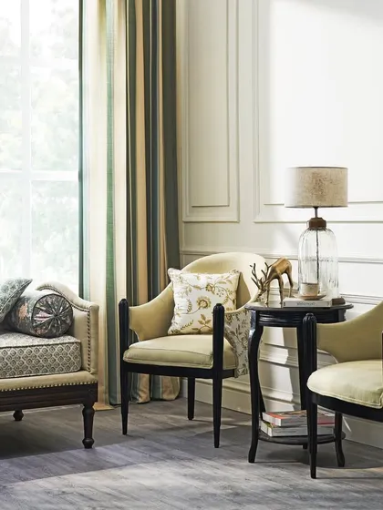 A neo-classical living room vignette with elegant armchairs and a daybed. The soft, natural light highlights the delicate patterns of the upholstery and the classic lines of the furniture.
