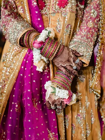 A close up of a bride's hands, showing her colorful bangles, intricate mehndi, and beautiful floral bracelets. This shot is all about the vibrant and detailed accessories of a mehendi ceremony.