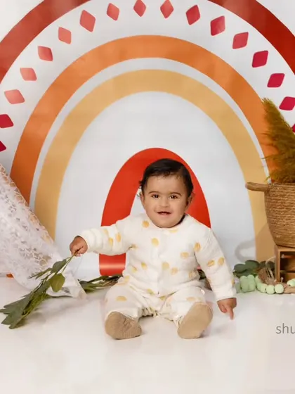 A happy baby sitting in front of a beautiful boho rainbow backdrop, a perfect theme for a cheerful soul.