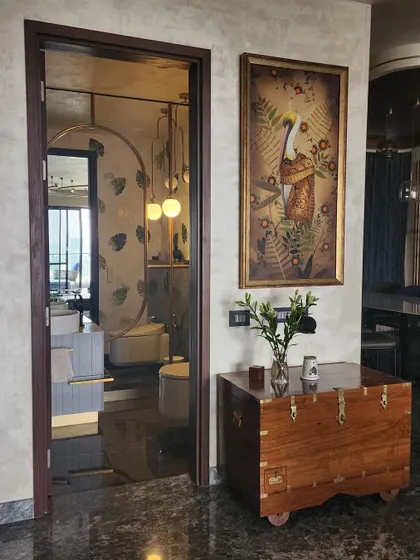 The entrance to the powder room, marked by a tinted glass door that offers a hint of the unique design within. A vintage wooden chest and nature-themed artwork in the hallway set a warm, artistic tone for the home.