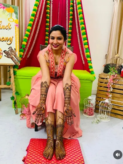 A happy bride proudly displaying her complete mehndi. The design is consistent across her arms and legs, showcasing a full and elegant bridal henna service.