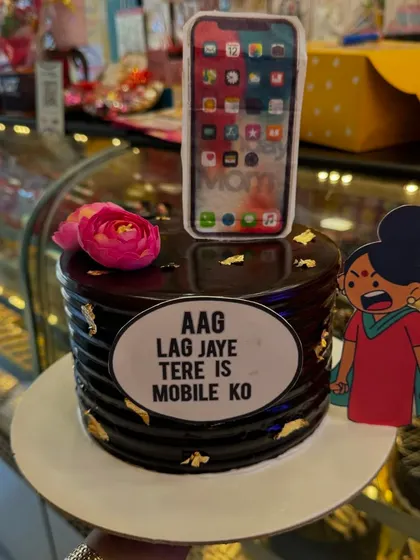 A funny and relatable cake for someone who is always on their phone. The design features an iPhone with an angry mom character saying "Aag lag jaye tere is mobile ko," a classic Indian mom dialogue.