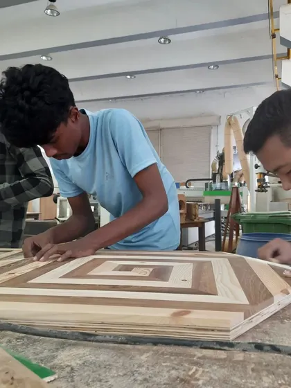 Students work on a complex tabletop featuring an intricate geometric inlay pattern, a project that requires advanced skills in precision cutting and assembly.