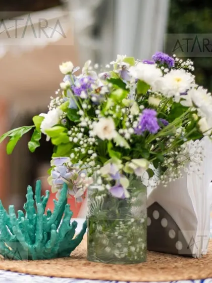 A close-up of a floral centerpiece at a nautical-themed party. The arrangement is placed next to a piece of teal-colored coral, perfectly blending floral beauty with the sea theme.