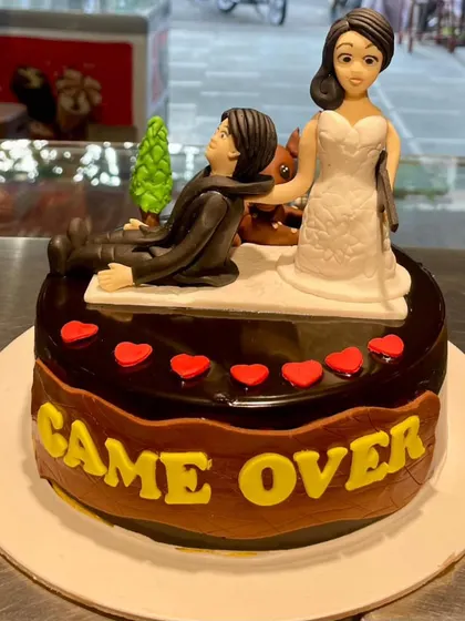 A humorous "Game Over" cake perfect for a bachelor party or a fun-loving couple. This chocolate cake features a playful bride and groom topper.